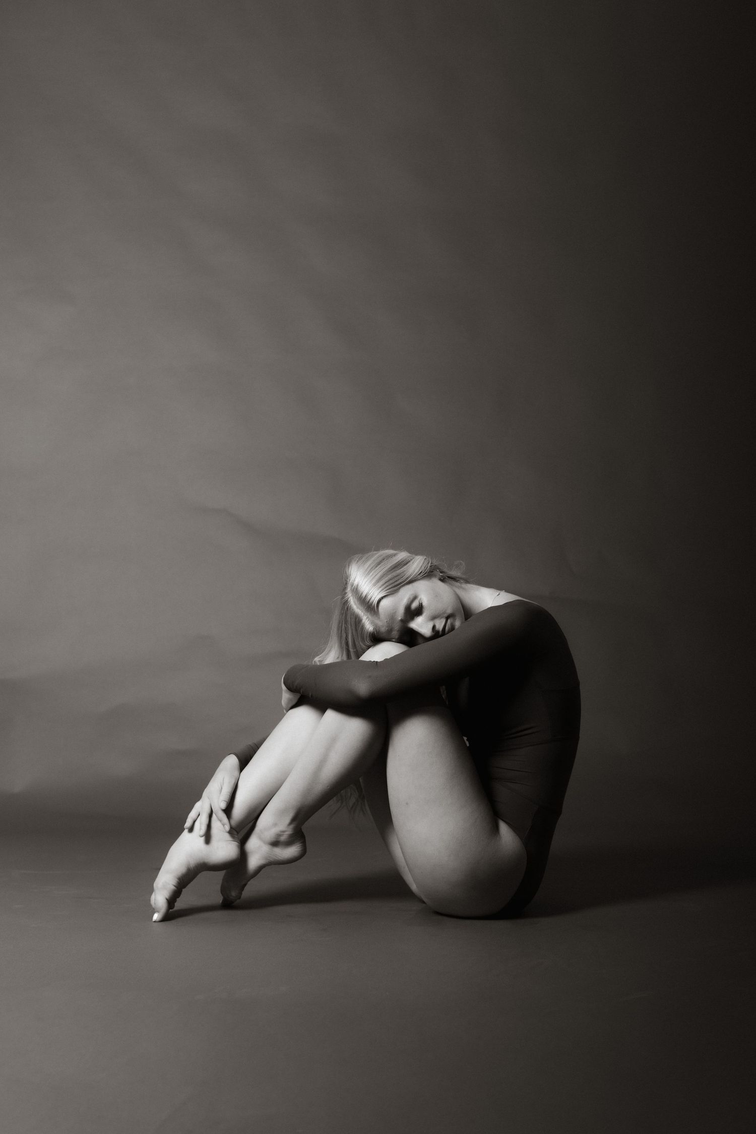 Black and white photo of a blonde ballerina in pointe shoes sitting curled up on studio floor on Ladys Island, Beaufort, SC.