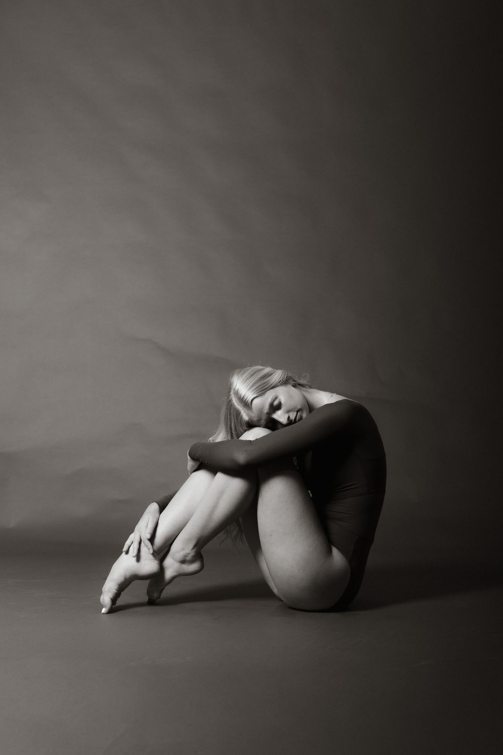 Black and white photo of a blonde ballerina in pointe shoes sitting curled up on studio floor on Ladys Island, Beaufort, SC.