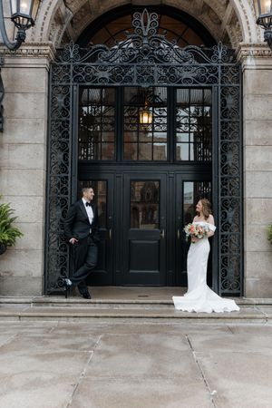 Bride and groom pose before ornate wrought iron gates and grand doors at an elegant wedding venue.