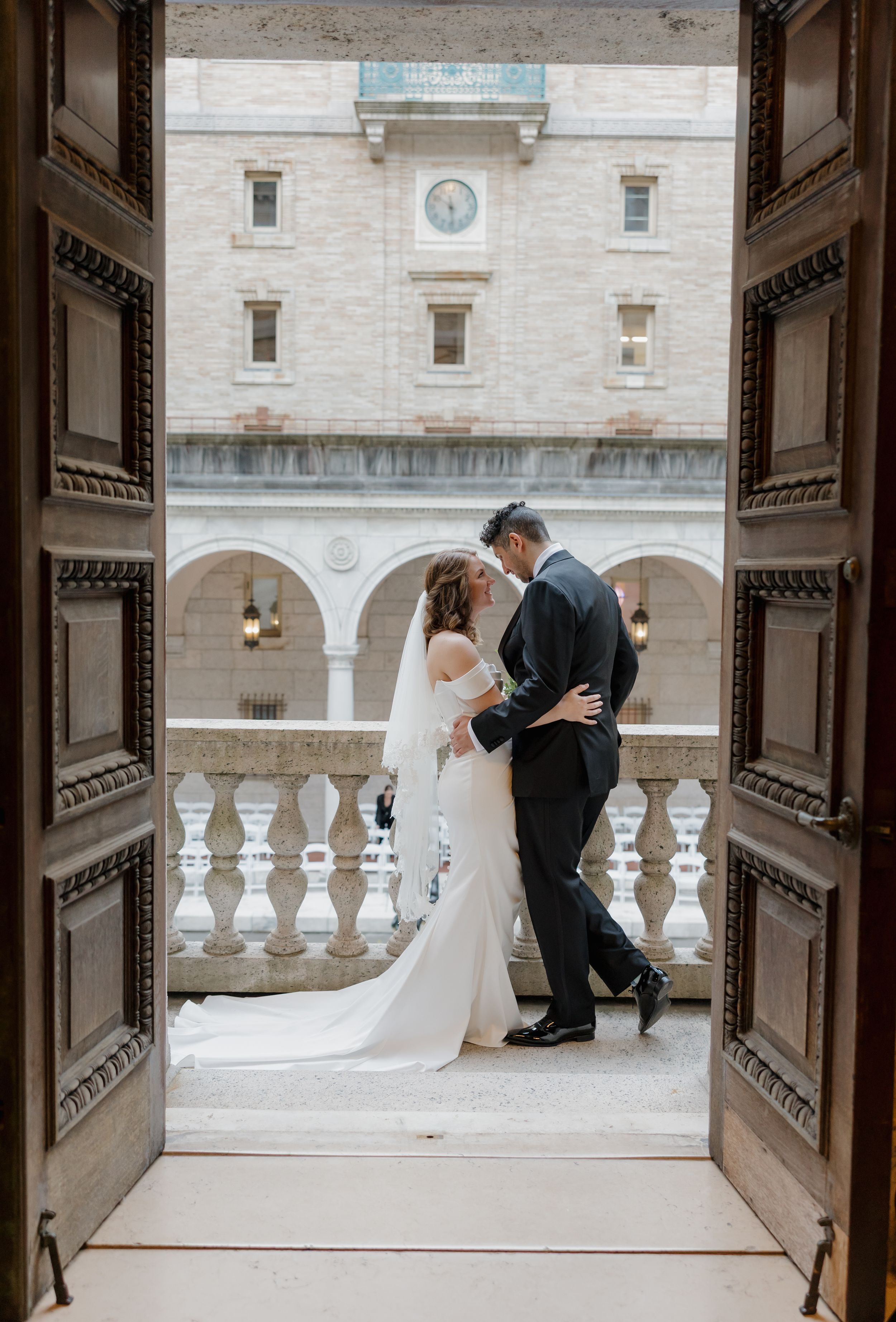 Bride and groom share a romantic kiss framed by ornate wooden doors at an elegant wedding venue.