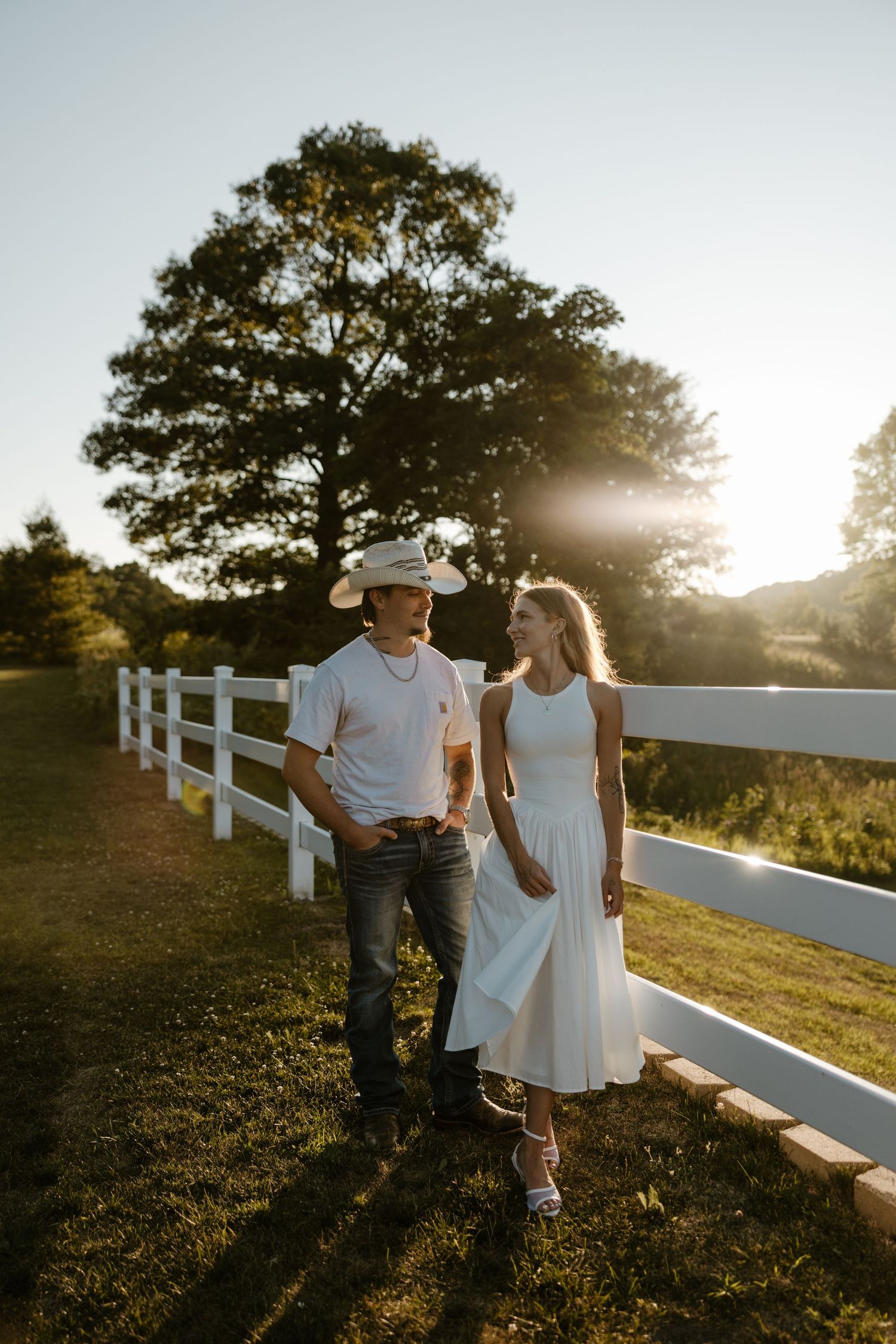 A couple walks together on a path surrounded by trees and fencing at sunset. Fort Worth Texas wedding photographer.