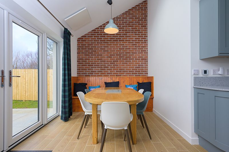 Modern open concept living space with exposed brick wall, sloped ceiling, and large windows letting in natural light.