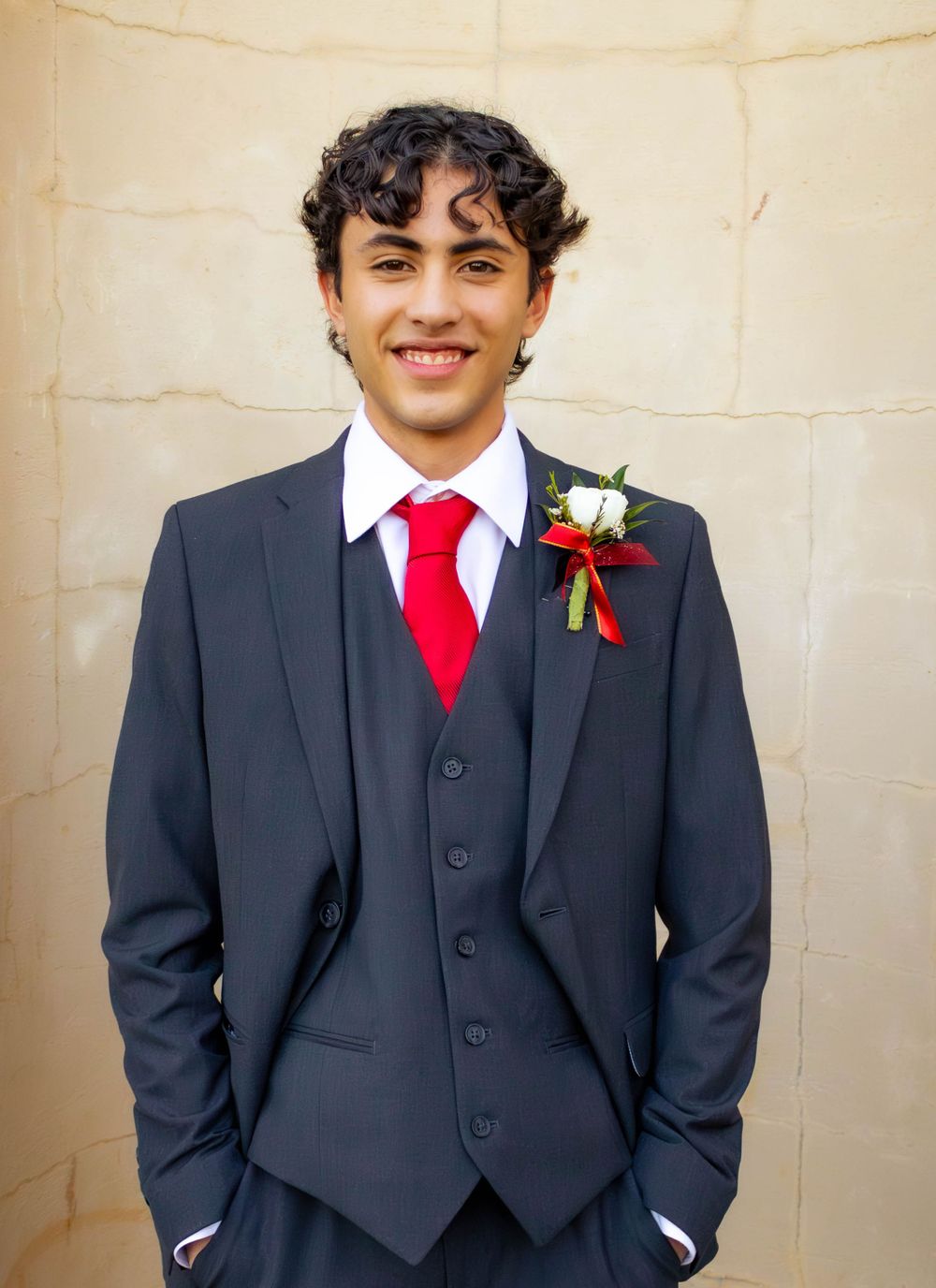 Young man in navy suit with red tie and boutonniere poses for formal portrait.