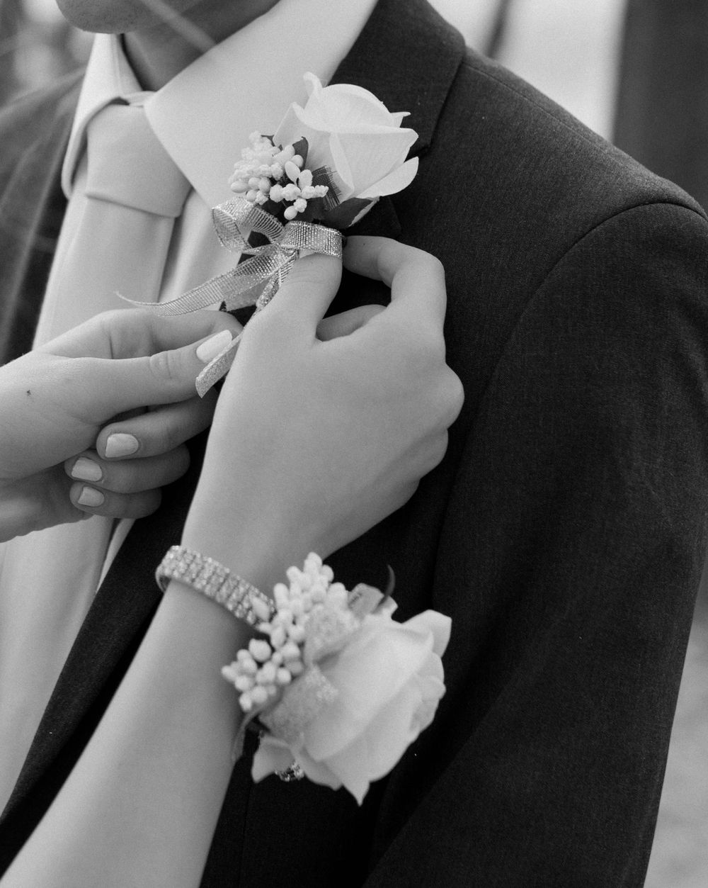 Black and white photo of hands pinning a boutonniere and corsage during a formal event.