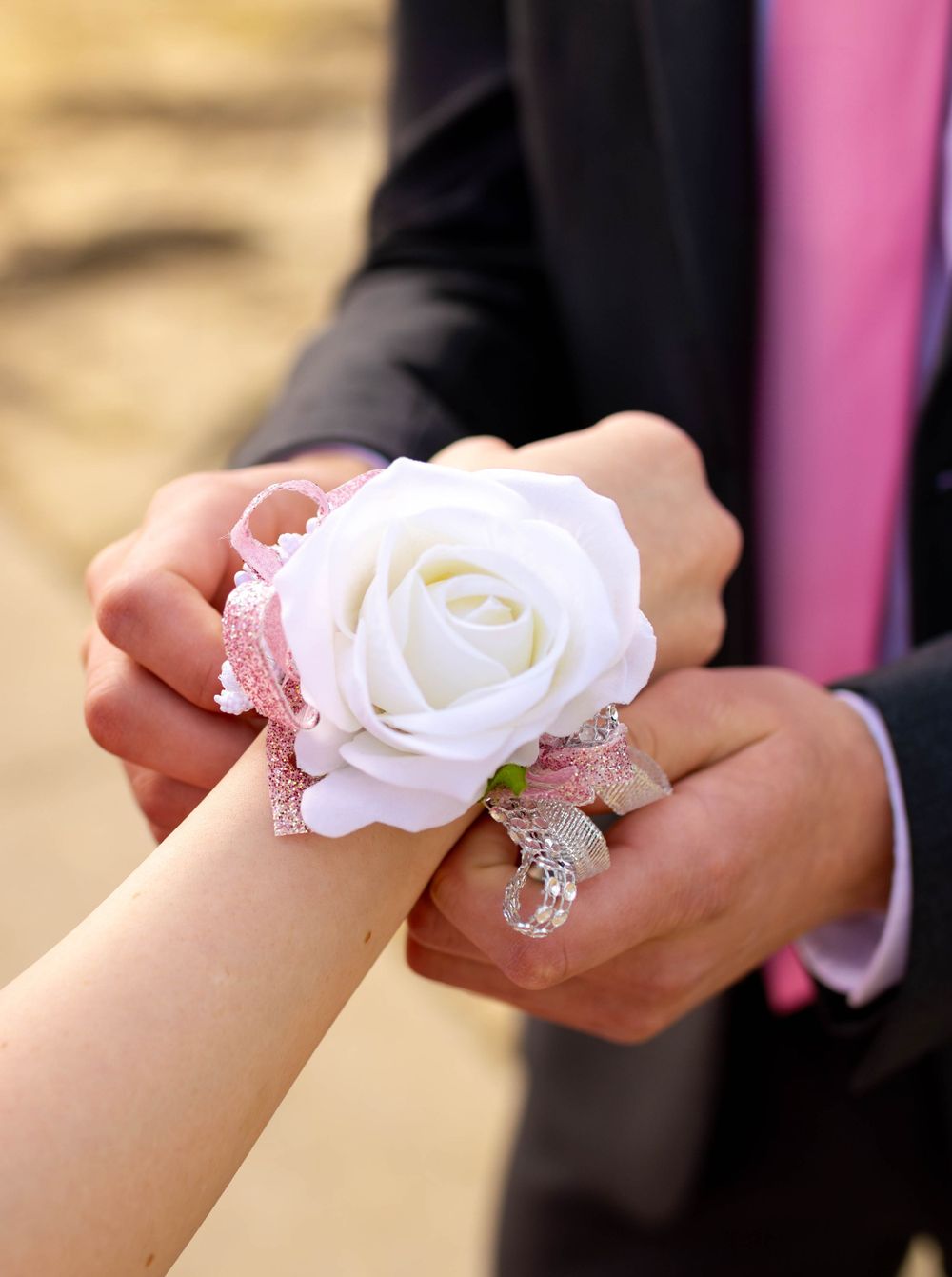 Close-up of hands placing a white rose corsage on wrist during formal event.
