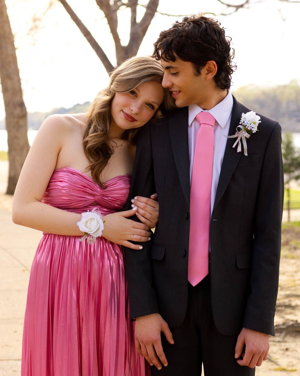 Couple in formal wear embrace outdoors, coordinating in pink dress and matching tie.