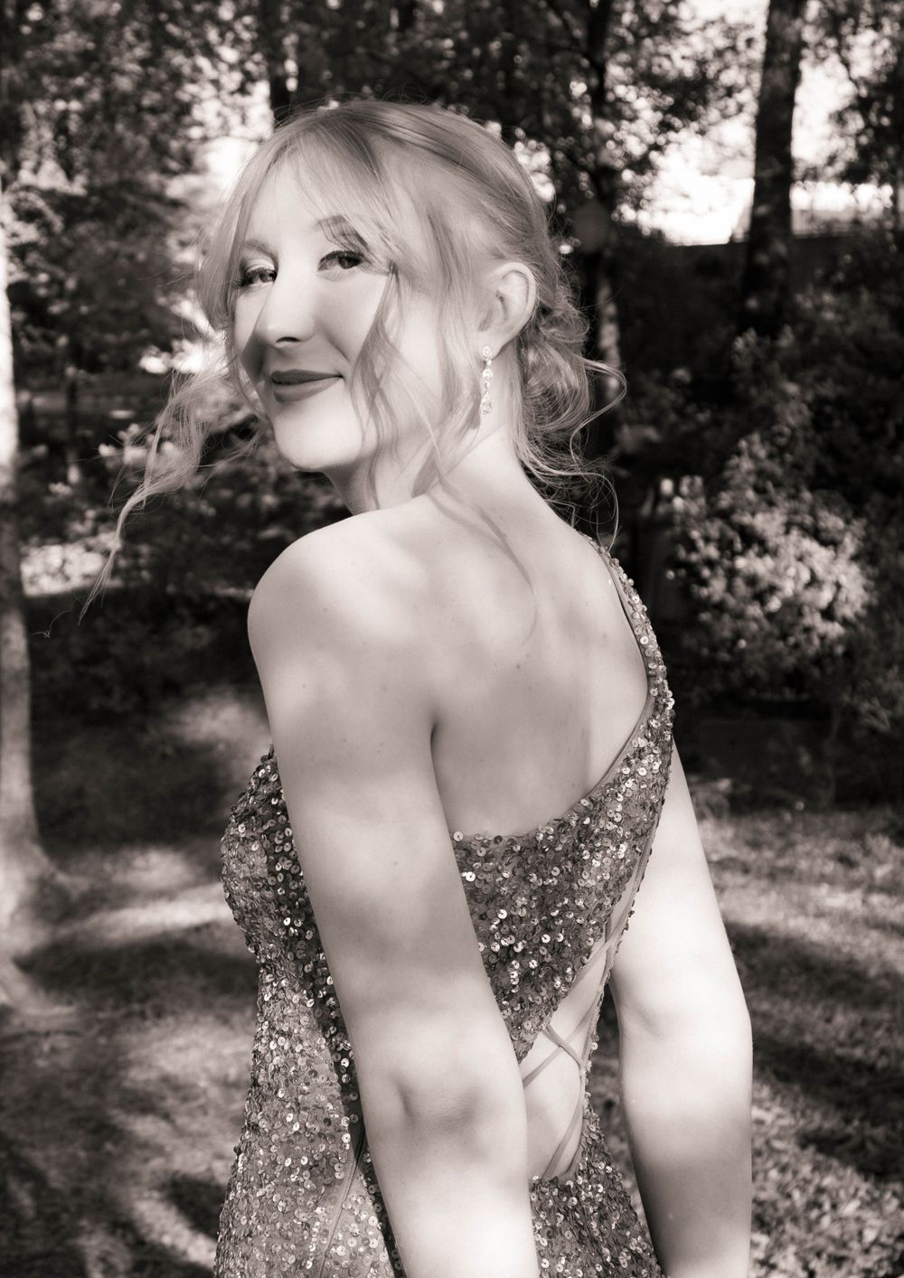 Black and white portrait in sparkly dress showing back pose outdoors.