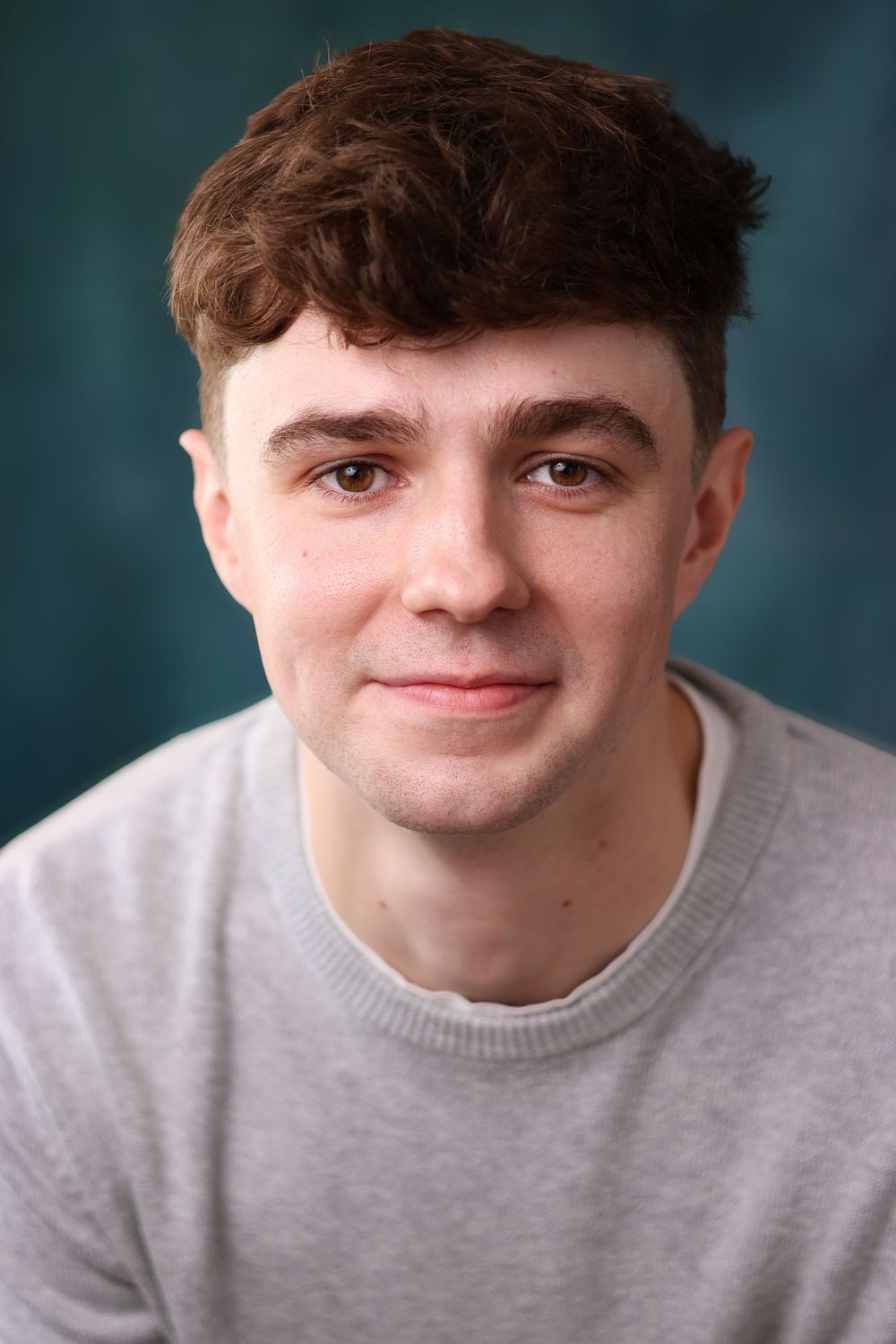 A series of four headshots showing someone in a light gray sweater with varying smiling expressions against a blurred background.