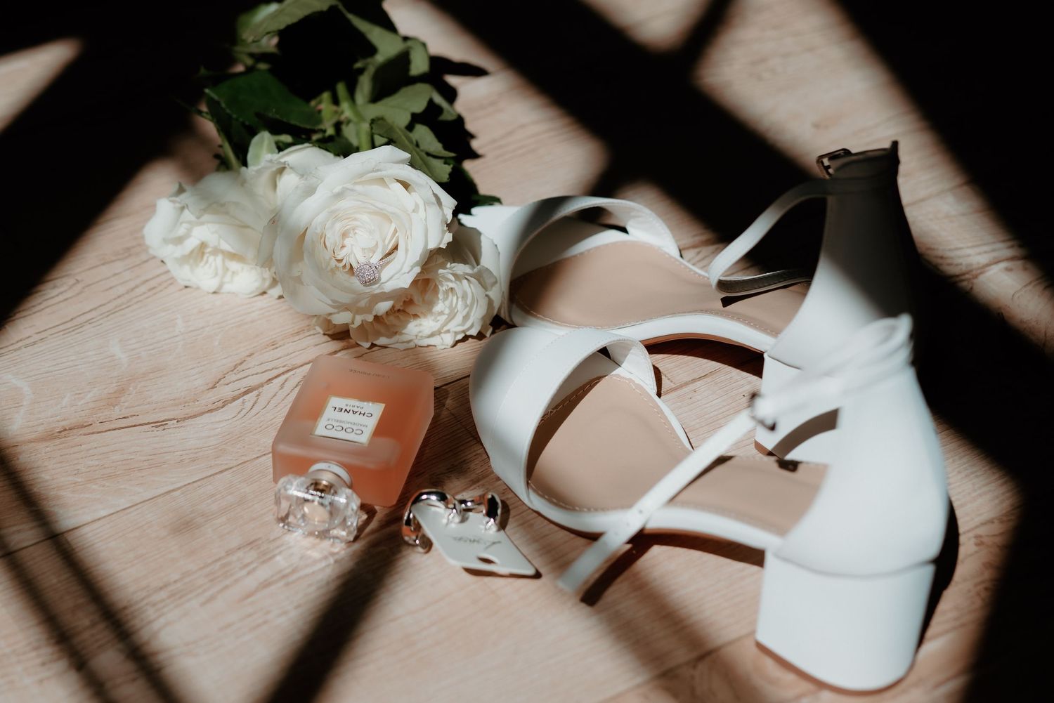 Wedding details including white roses and bridal shoes arranged with dramatic lighting and shadows.