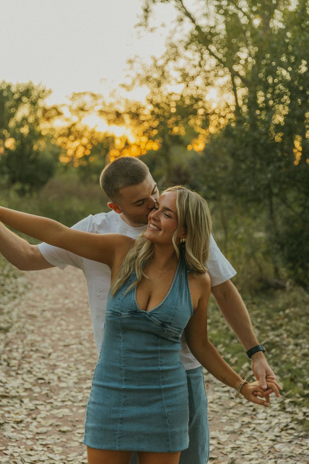 A playful couple dances and embraces in a field during sunset.