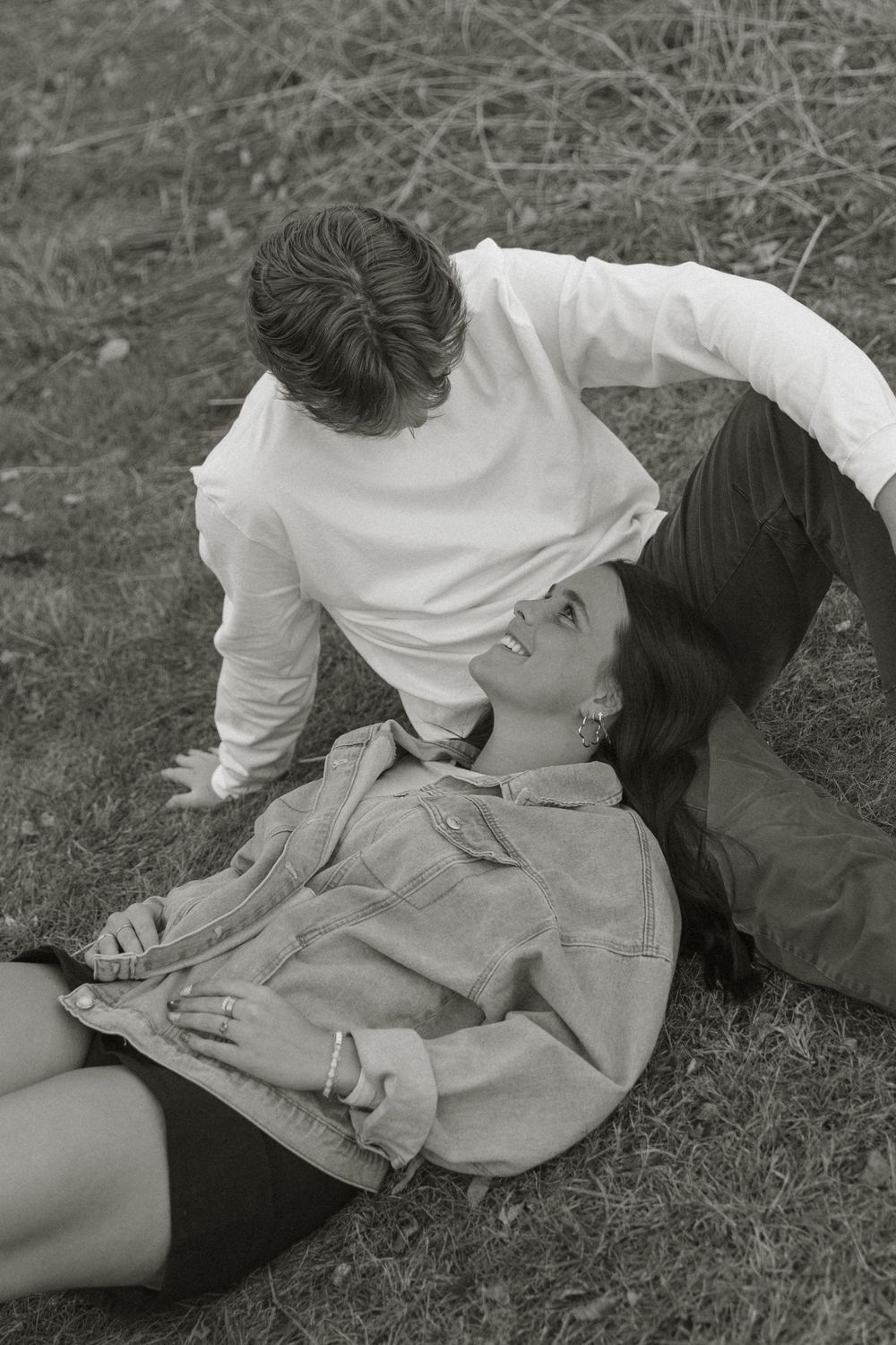 Black and white artistic photo of a couple lying in grass during a casual photoshoot.