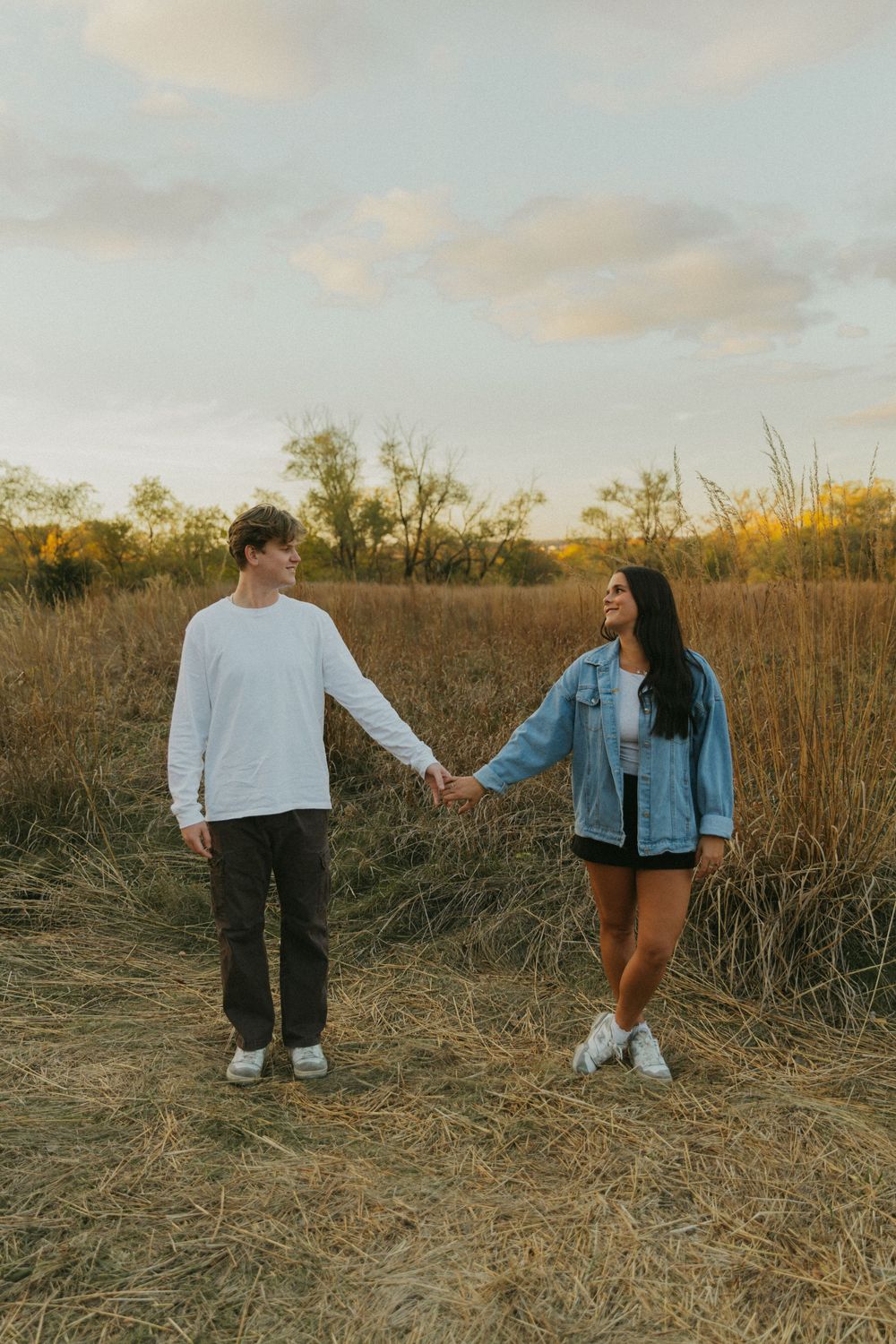 Couple in casual attire sharing playful moments in a rustic field setting.