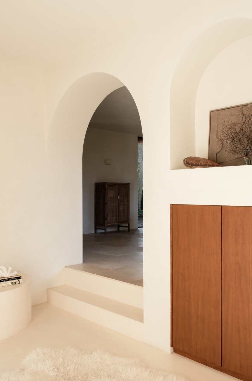 View through open wooden doors onto a sunny Mediterranean balcony overlooking terracotta rooftops in a historic town.