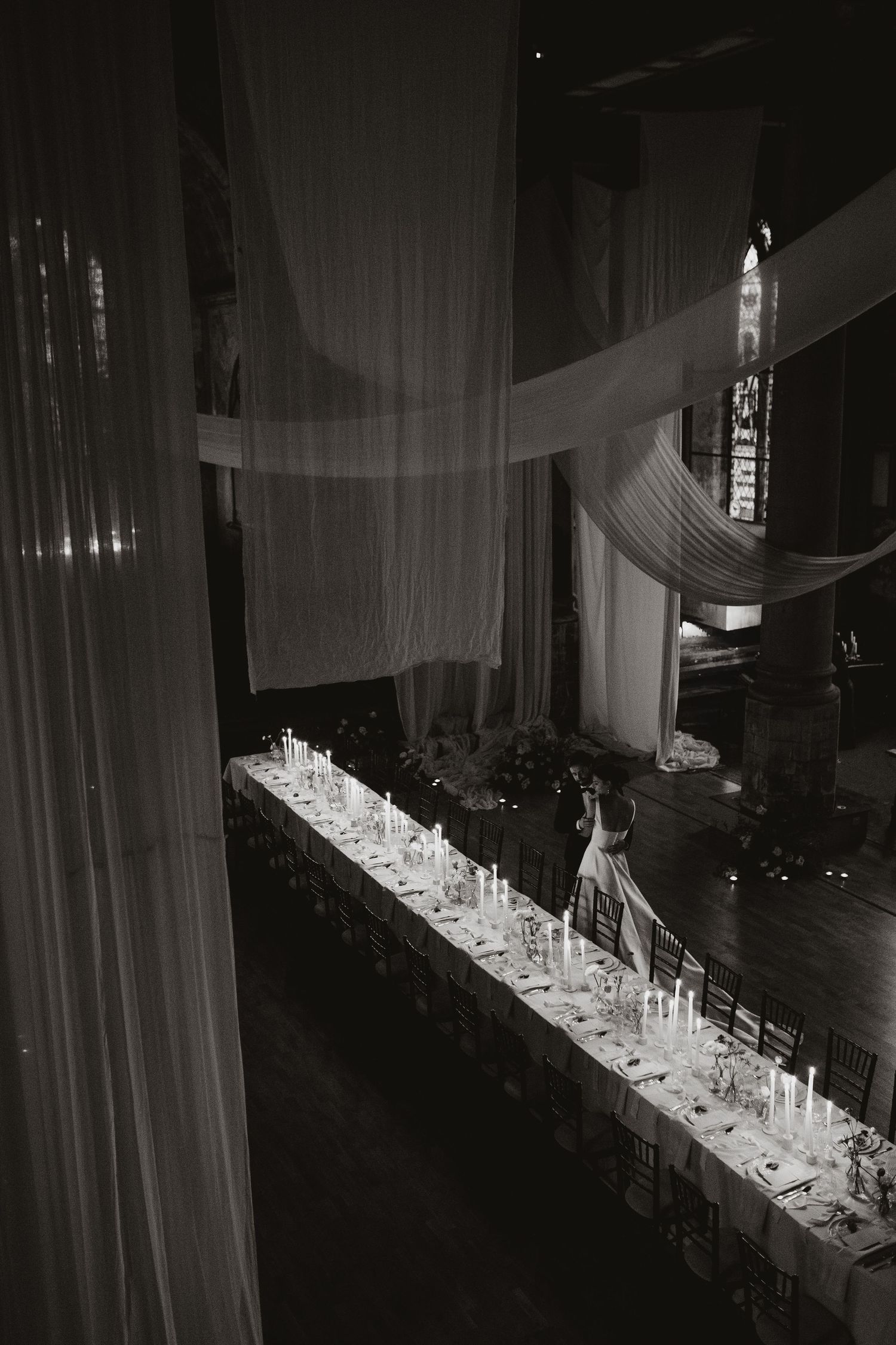 Aerial view of an elegant long banquet table with white linens and candlelight.