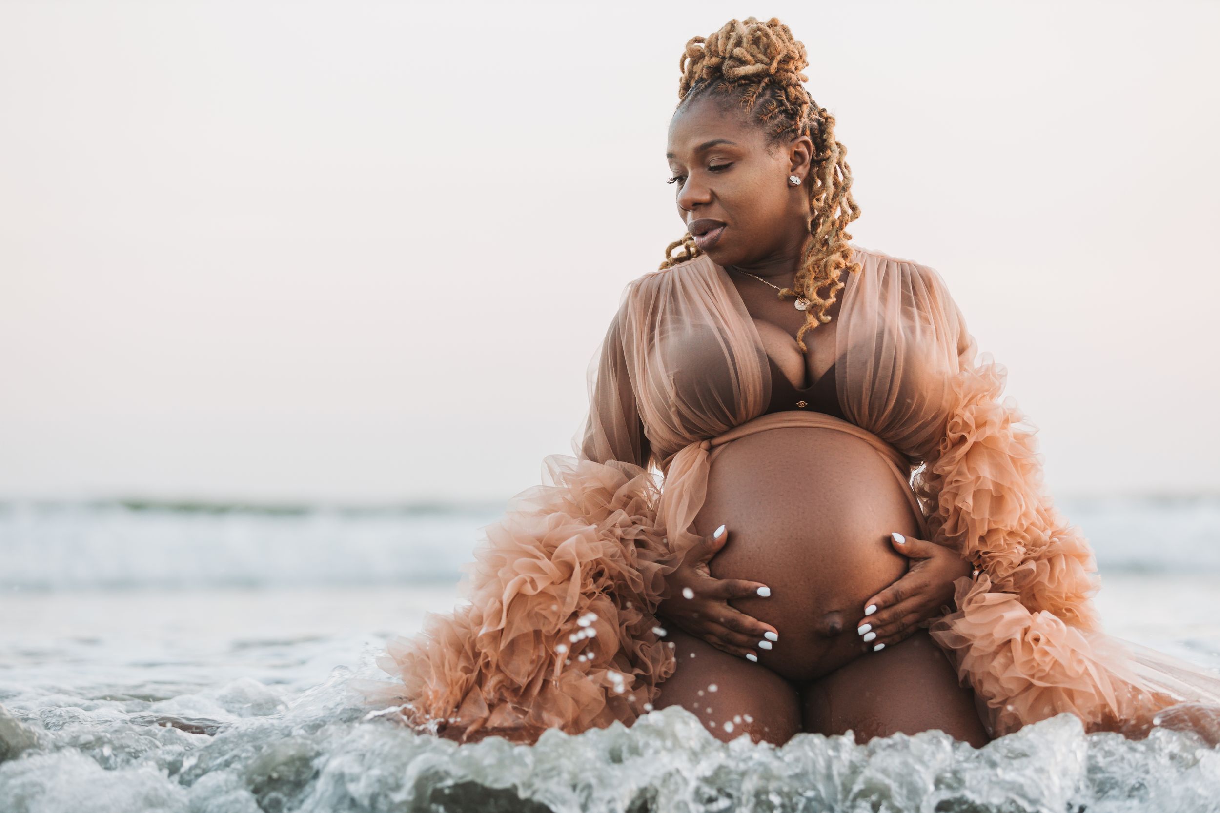 Maternity photo shoot on beach with mother wearing peach feathered gown.