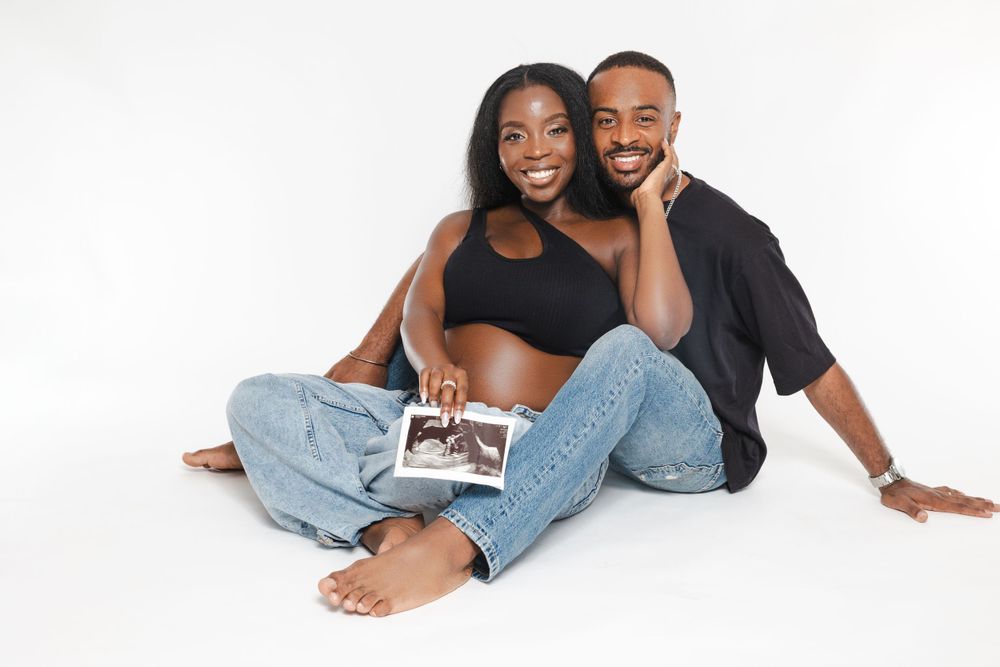 Couple sitting casually on white background holding ultrasound photo.