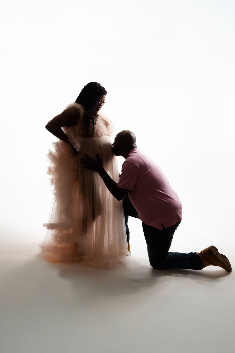 Silhouette of expectant couple in tender moment with flowing dress creating dramatic effect.