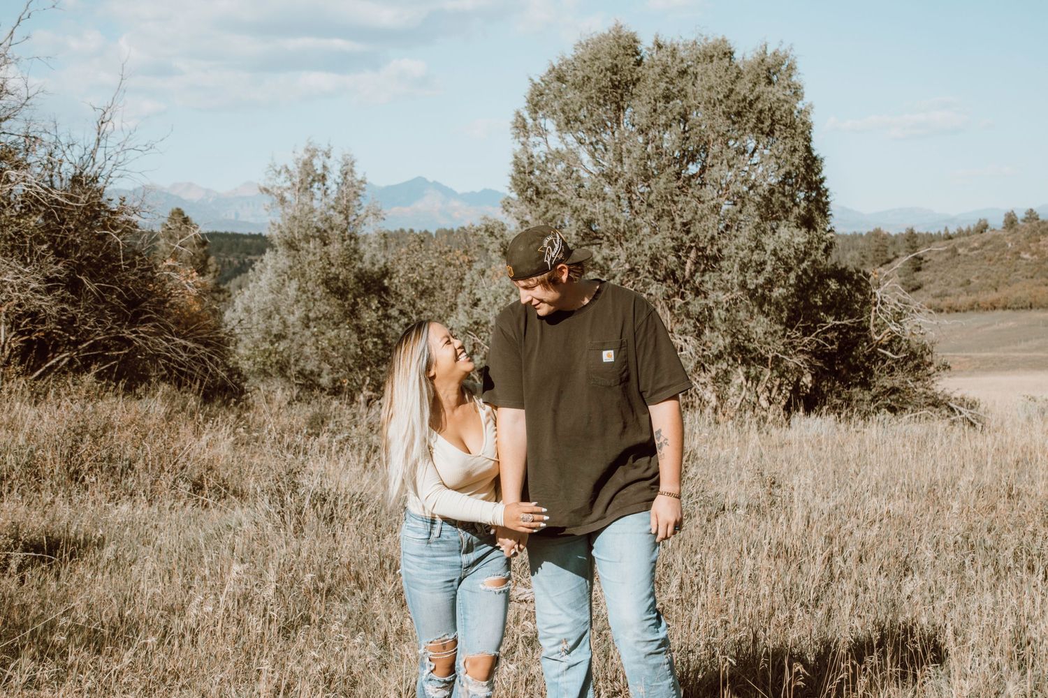 A couple embracing in a sun-drenched field with mountains in the background.