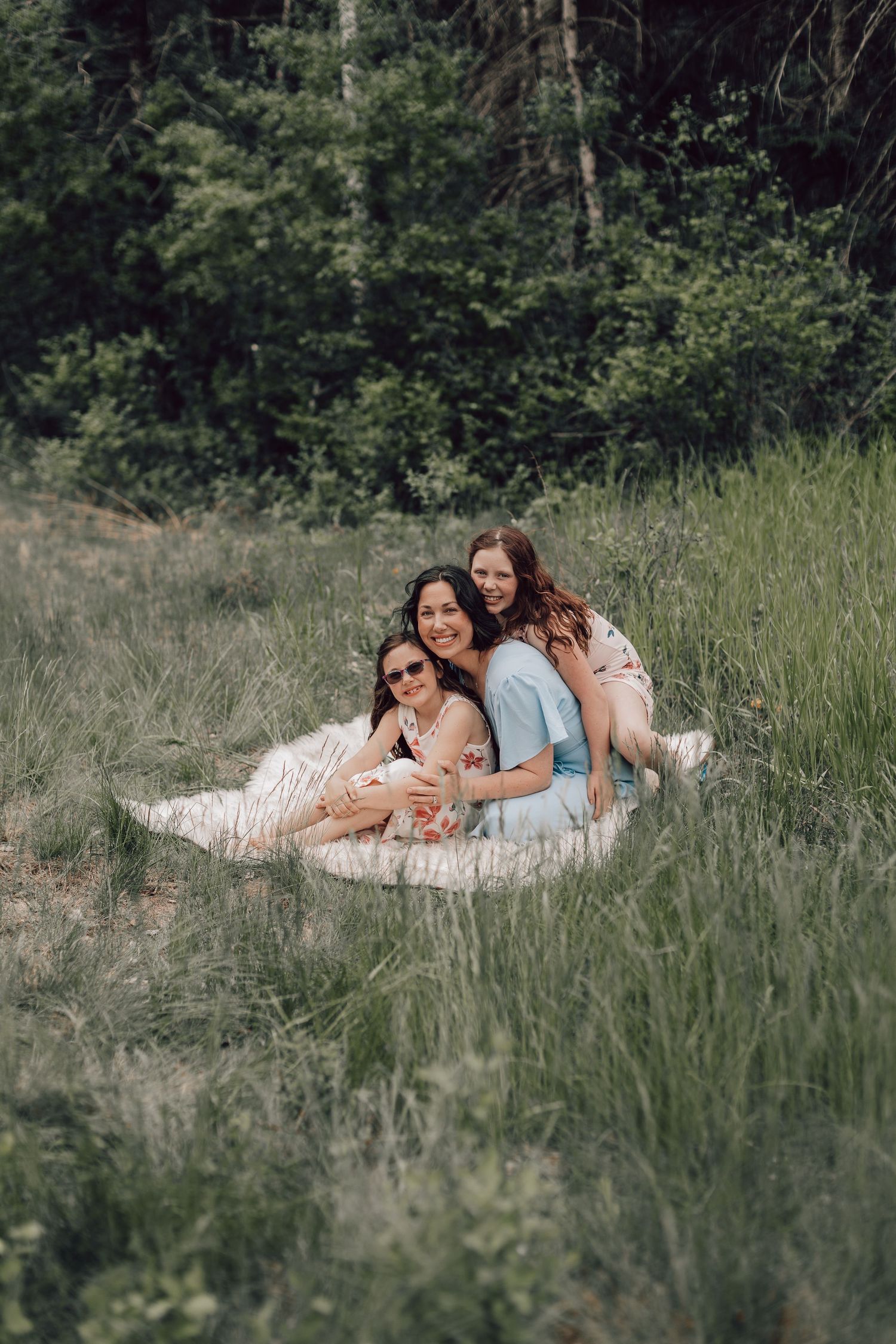 Three young women laughing and relaxing together on a blanket in a lush green field.
