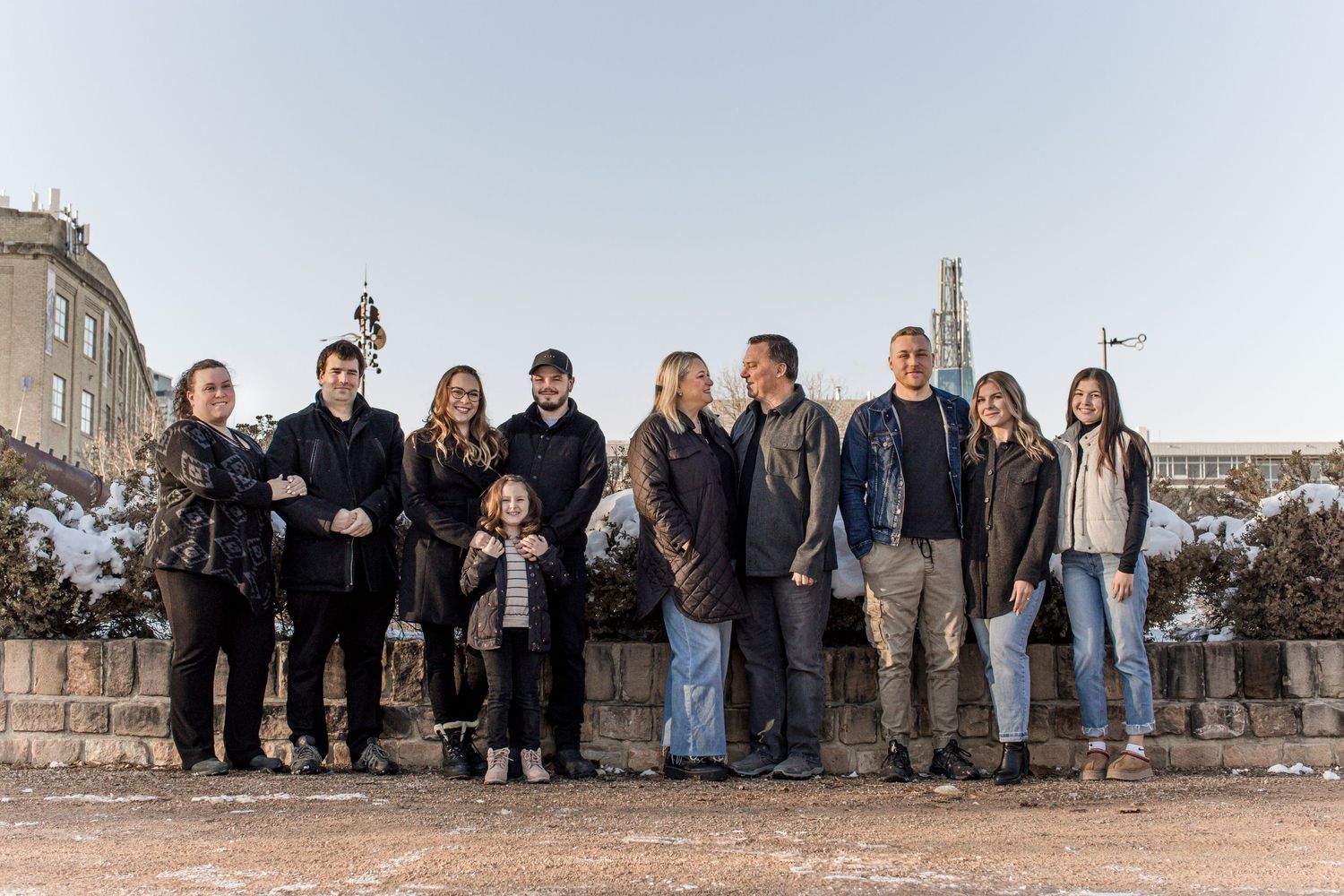 A large extended family posing together outdoors in winter with a city skyline backdrop.