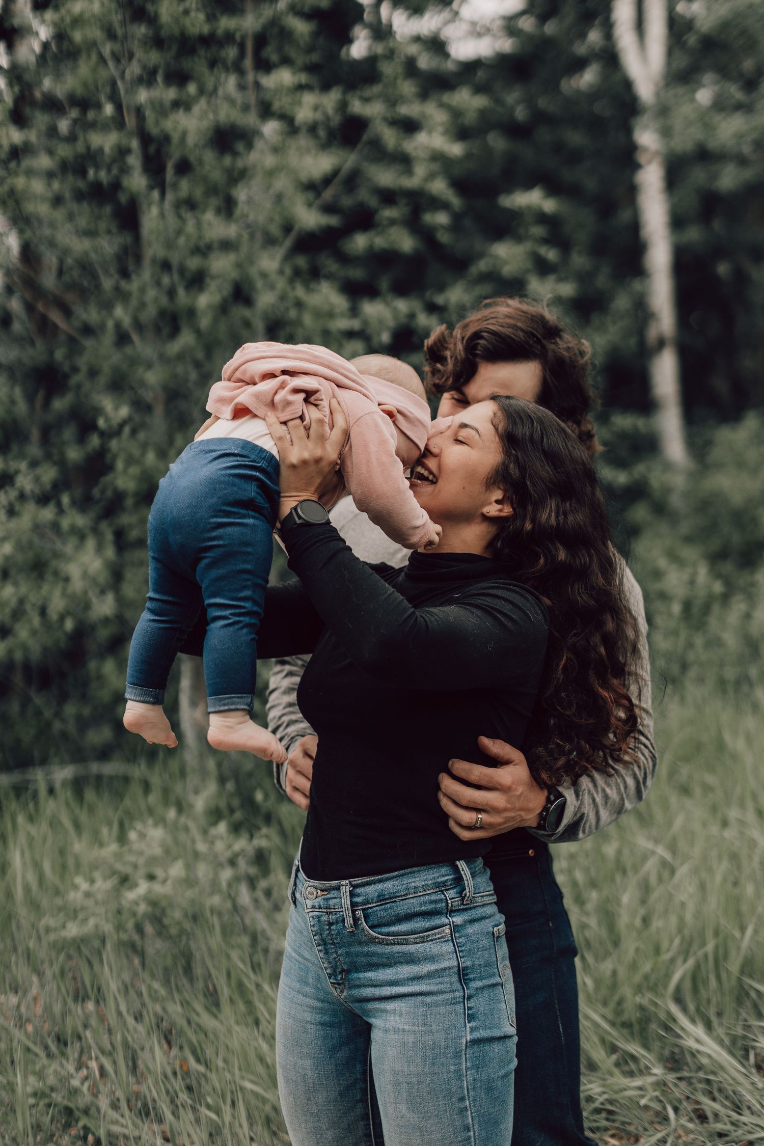 Joyful mother lifting smiling baby in lush green outdoor setting.