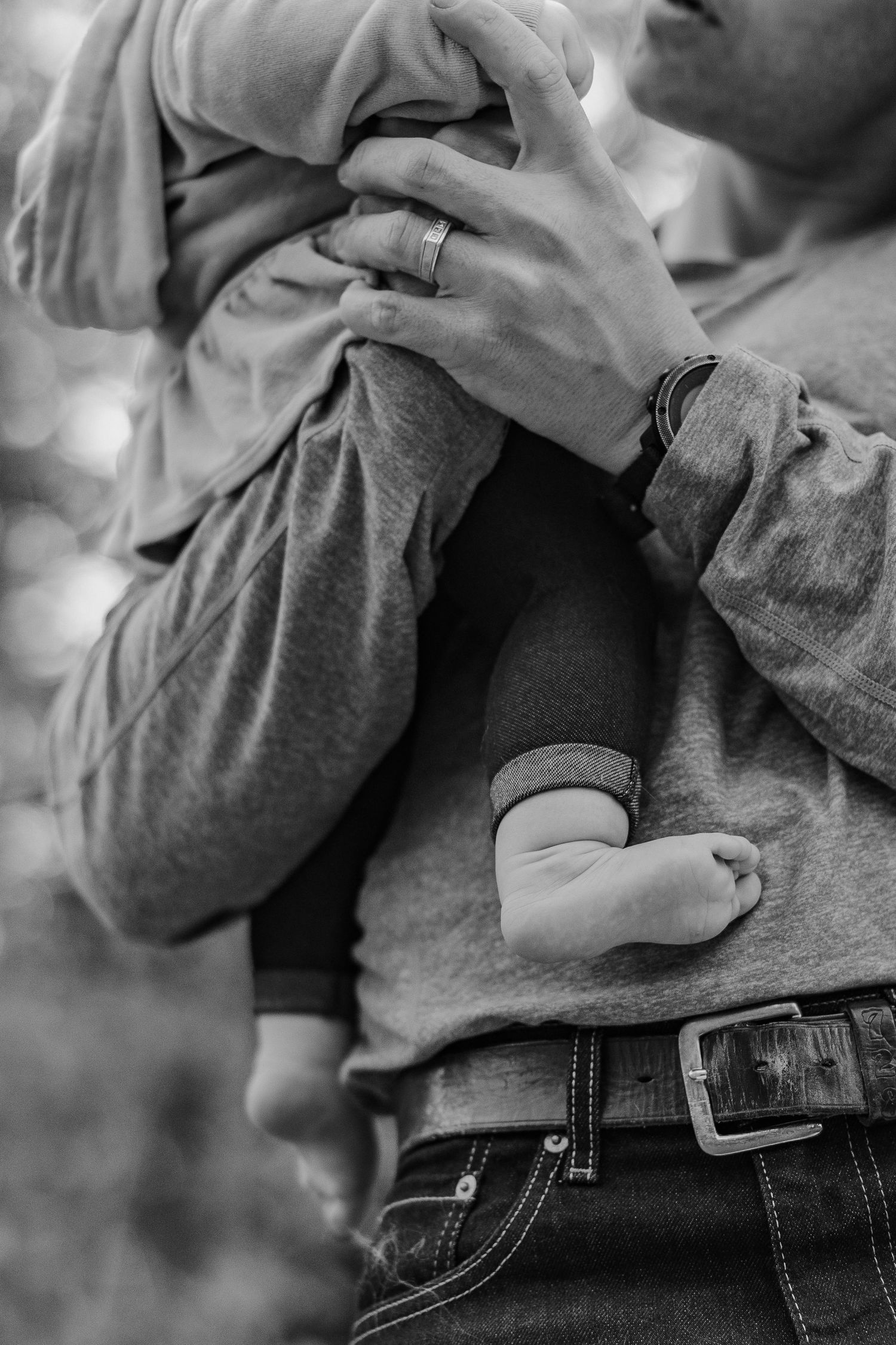 Black and white close-up of father holding newborn baby with wedding ring visible.