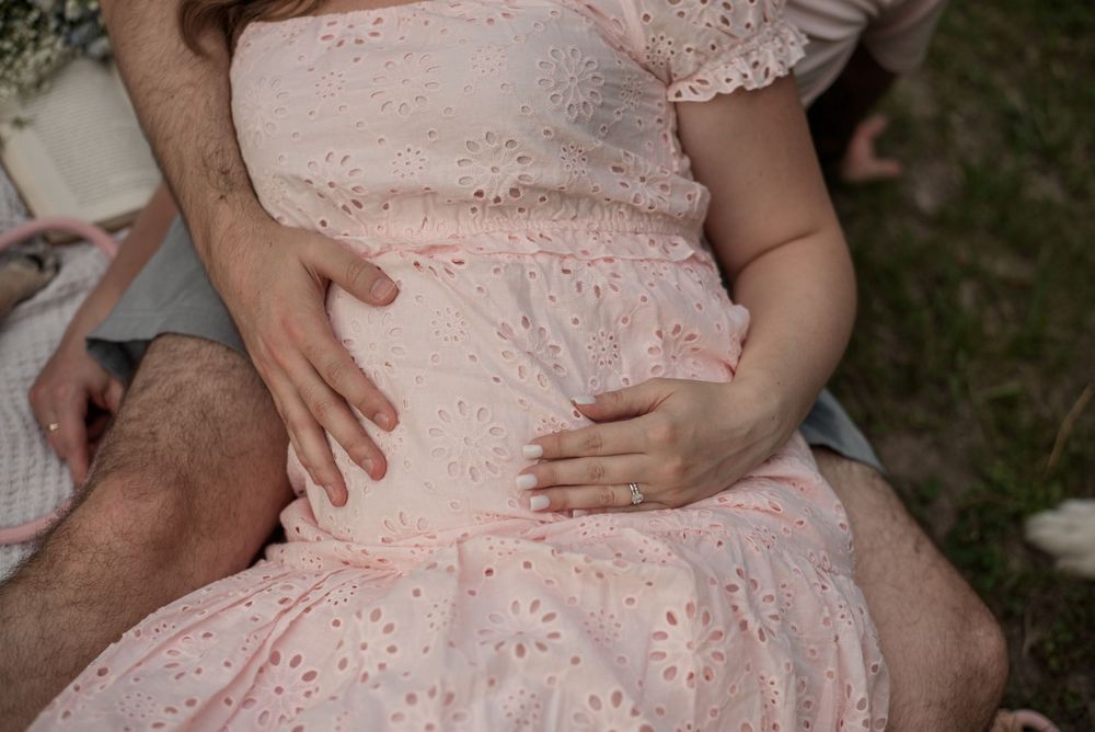 Pregnant woman in pink eyelet dress cradling baby bump outdoors during maternity photoshoot.