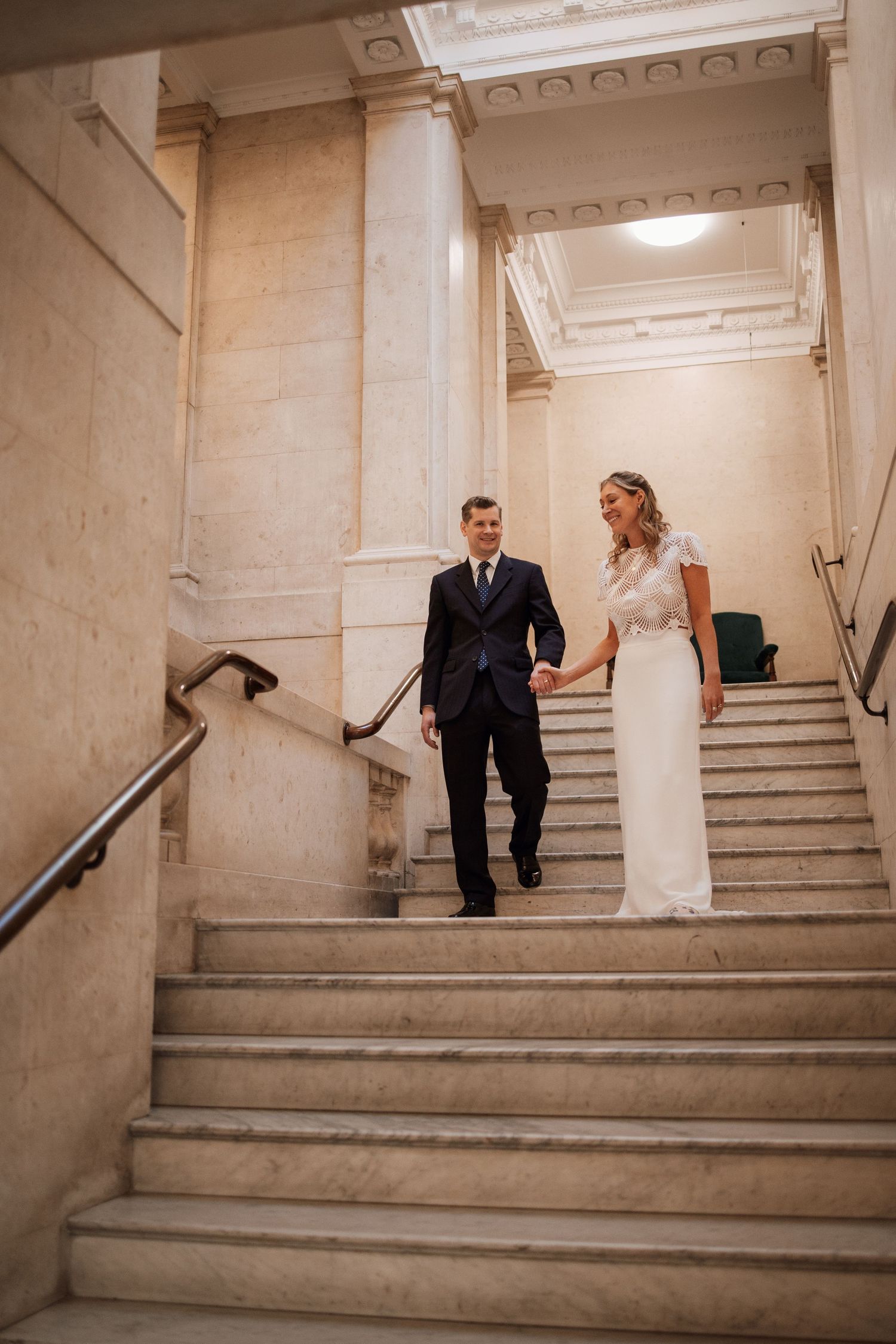 Sequence of a couple descending marble stairs in a classical building interior.