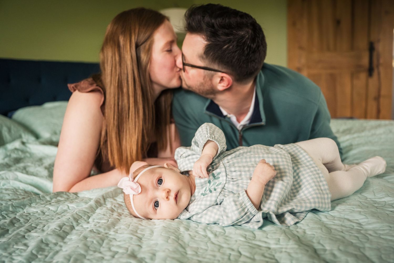 Father lying on bed laughing as young daughter climbs on him in cozy colorful bedroom.