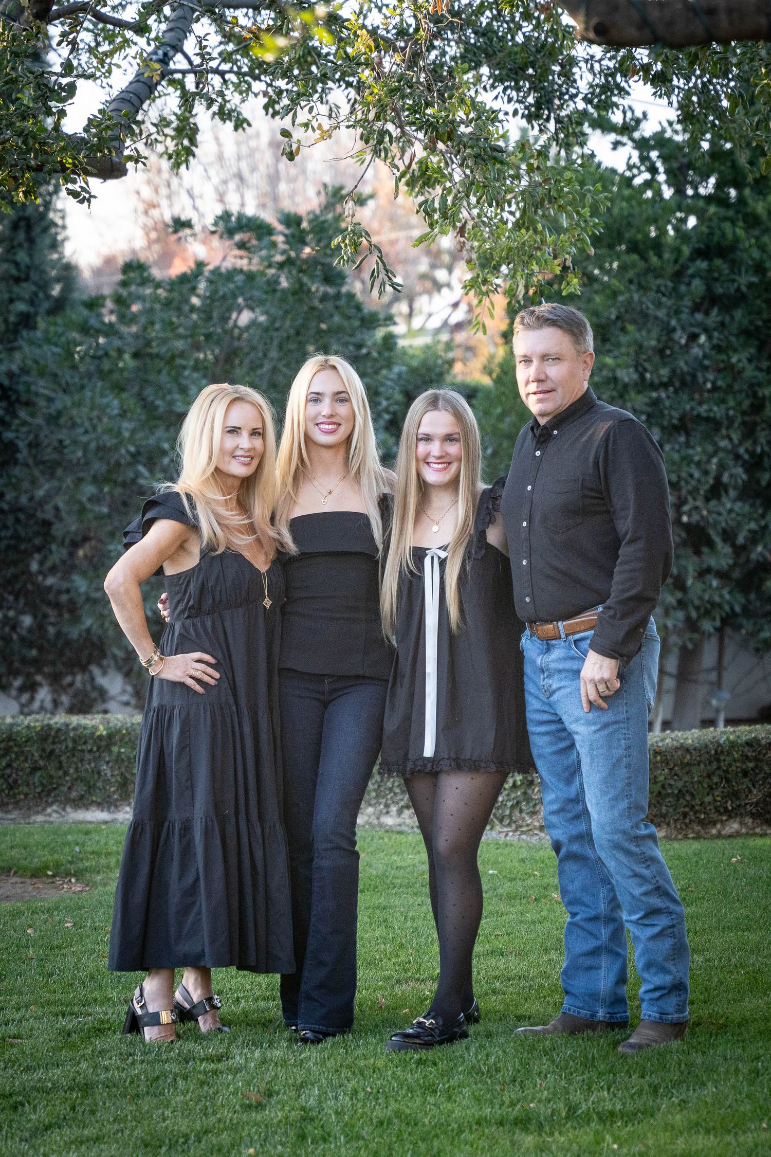 A family group poses together in casual attire on a backyard lawn near hedges.