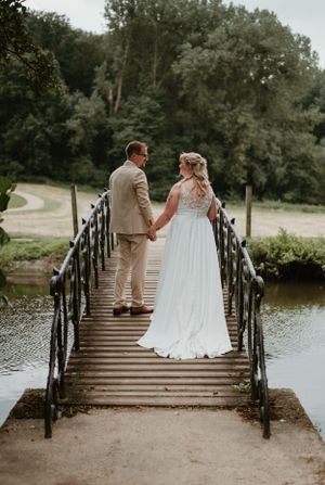 Een koppel in huwelijkskleding houdt elkaars hand vast terwijl ze op een brug staan, op park Ter Rijst, foto door Lien Photography.