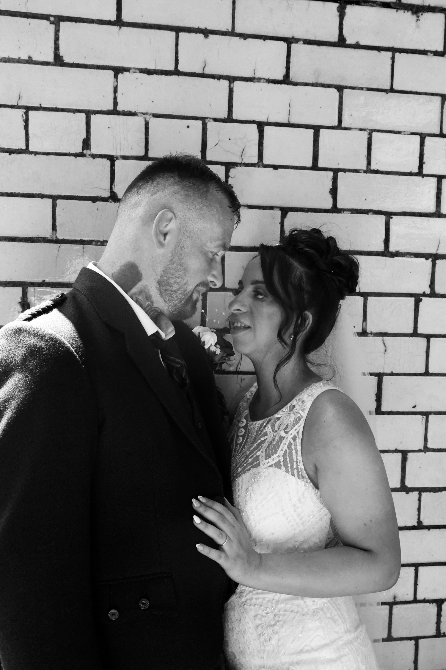 Black and white intimate portrait of newlyweds against brick wall.