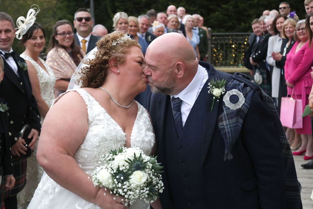 Wedding couple shares romantic moments in an outdoor garden setting with guests looking on during their celebration.