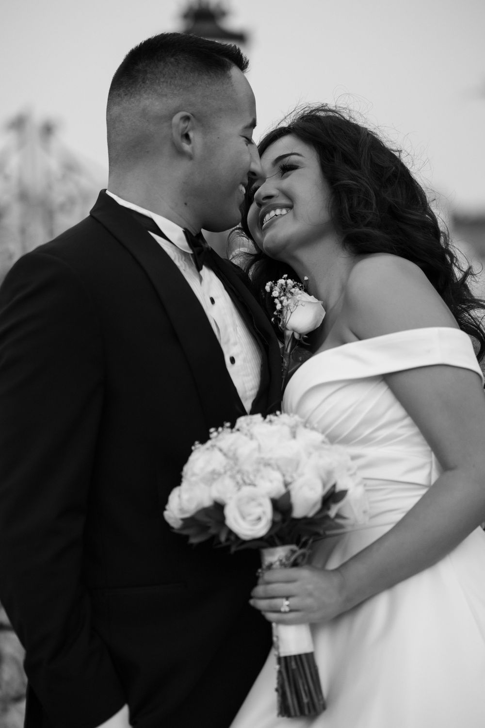 Black and white portrait of newlyweds sharing an intimate moment with bride holding white roses.