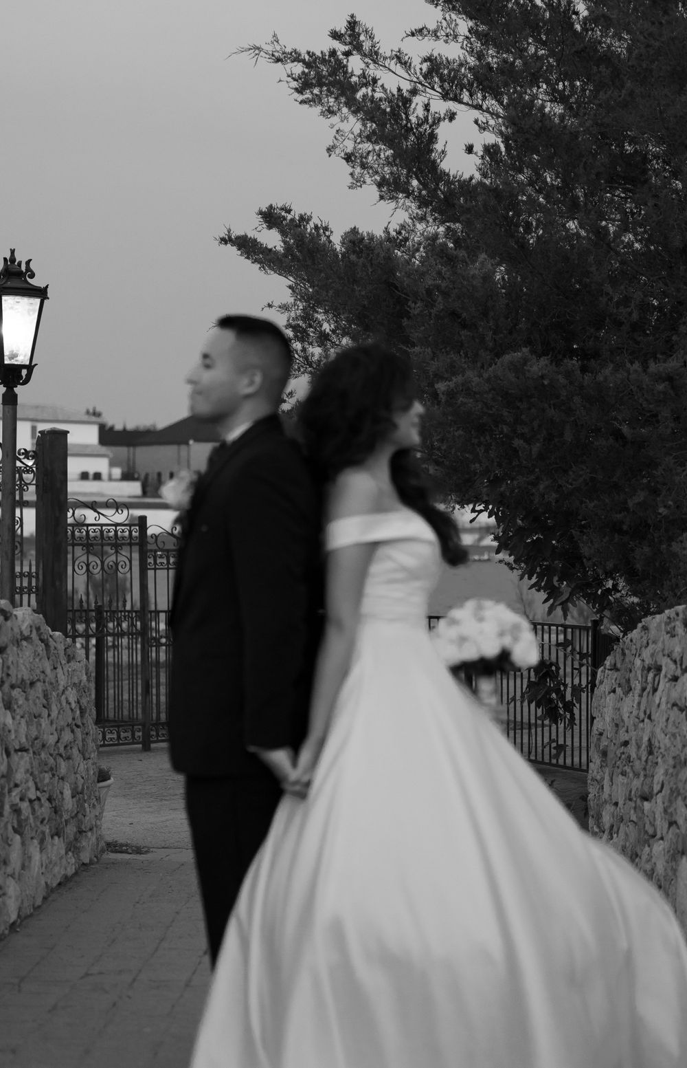 Black and white silhouette of newlyweds on stone pathway with lamp post.