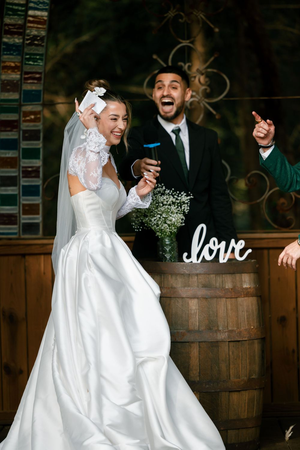 A joyous wedding celebration in front of a rustic wooden barrel with a white 'love' sign and baby's breath decorations.