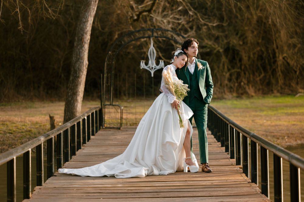 A romantic wedding couple stands together on a wooden bridge in a natural outdoor setting with a flowing white gown.
