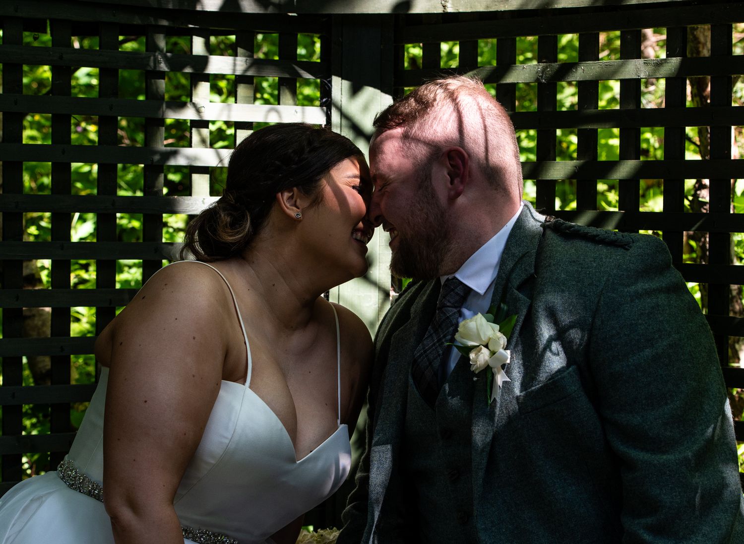 A joyful candid wedding moment shared between newlyweds in front of a lattice garden backdrop.