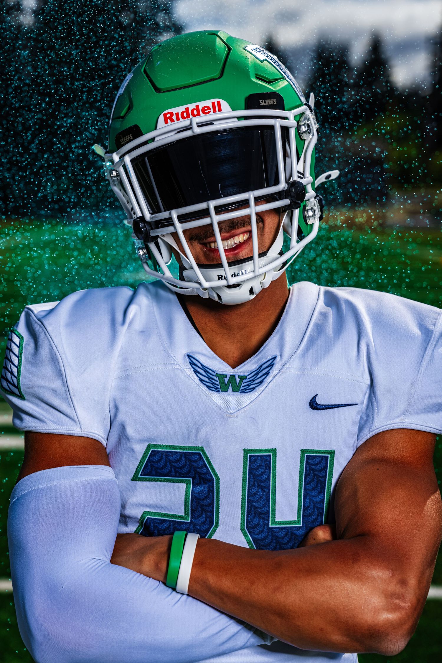 Football player in white jersey number 34 poses in green Riddell helmet with arms crossed during outdoor photo session.