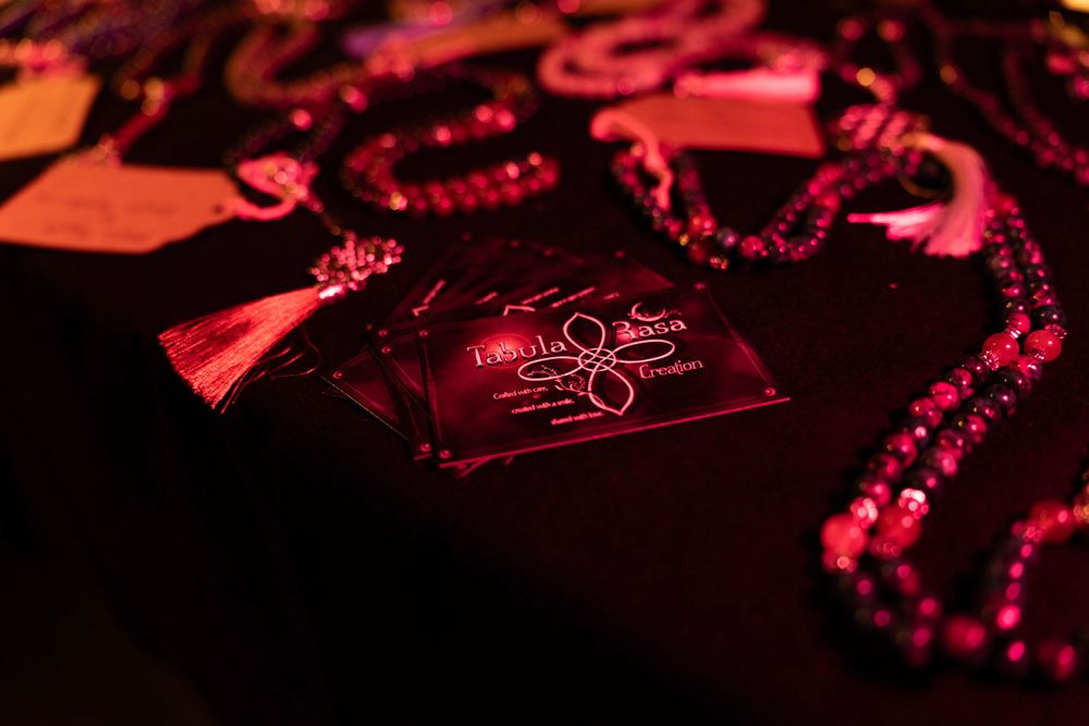 Close-up of beaded jewelry and necklaces laid out on a dark table, illuminated by warm, ambient light.