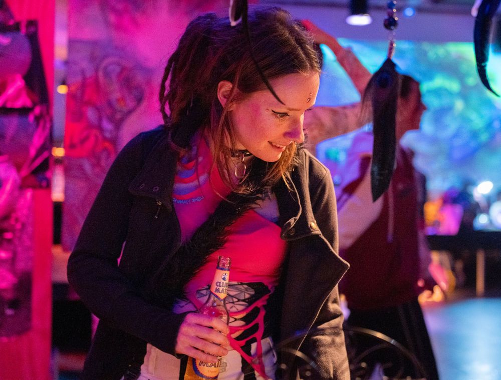 portrait of a woman at a psy party rave, shopping at the art markerplace with a colorful garland in a dark green setting. modem