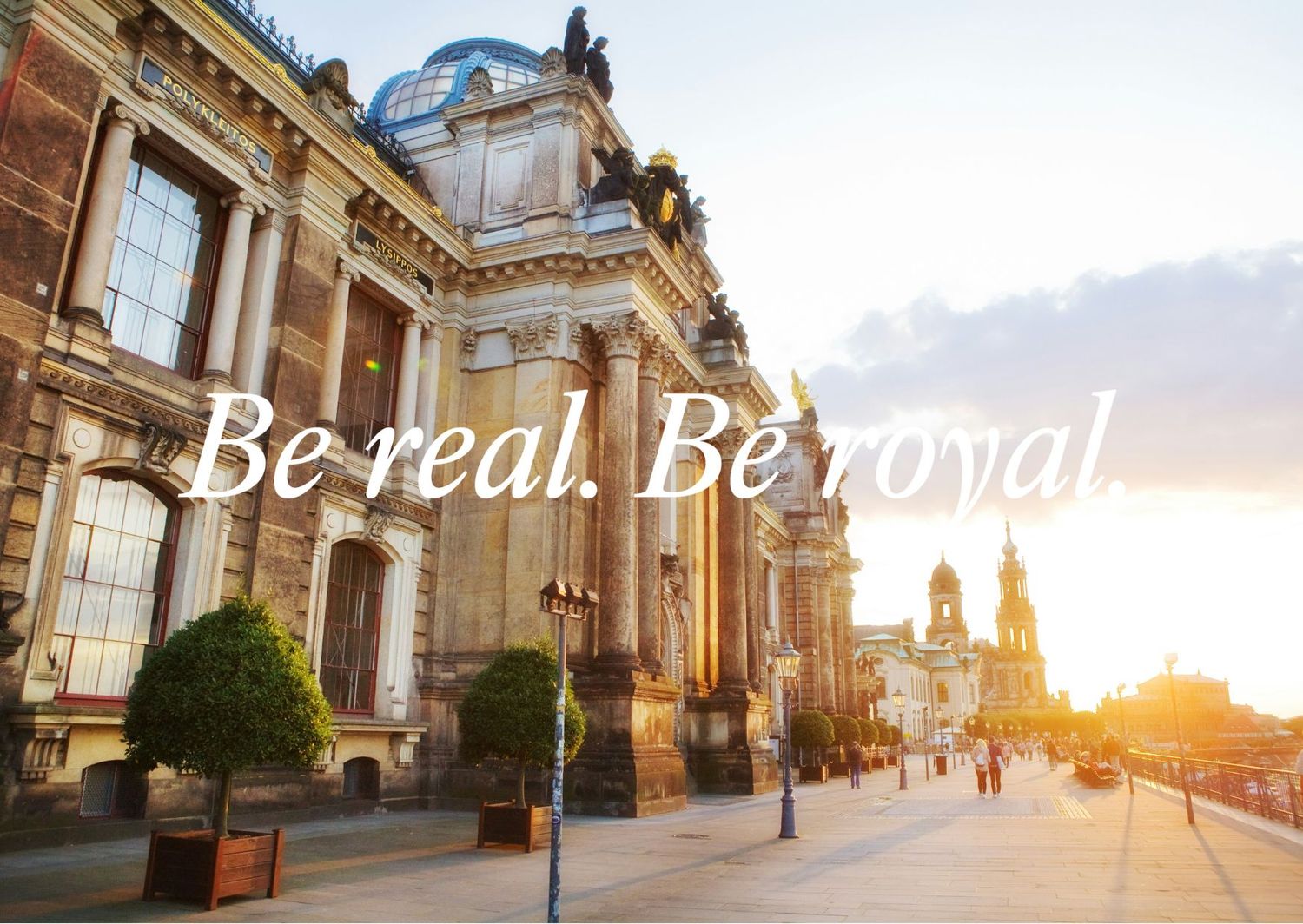 Historic building facade at sunset with 'Be real. Be royal' text and spires in background.