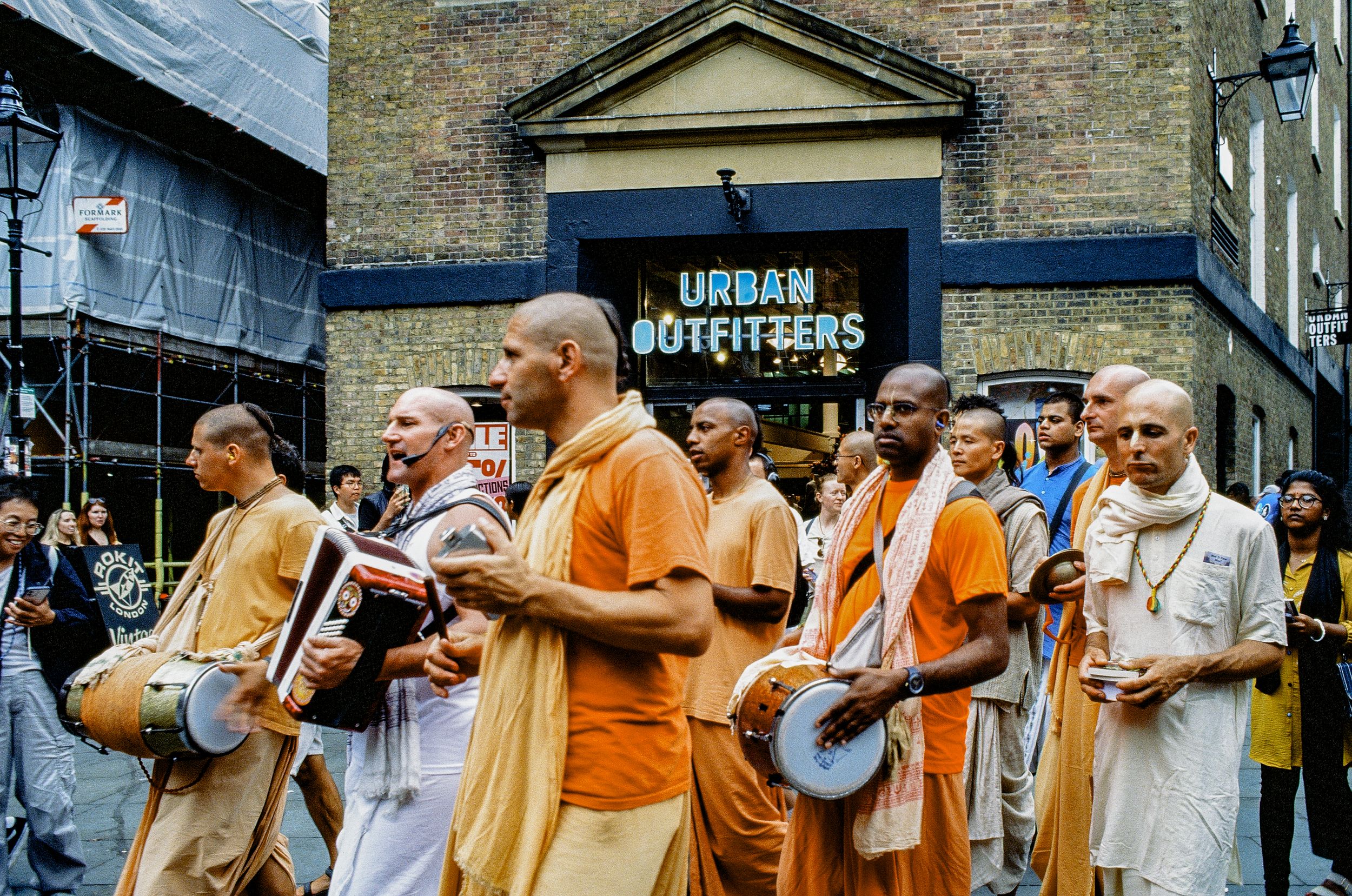 Group of Hare Krishna devotees in orange and white robes walking down a London street.