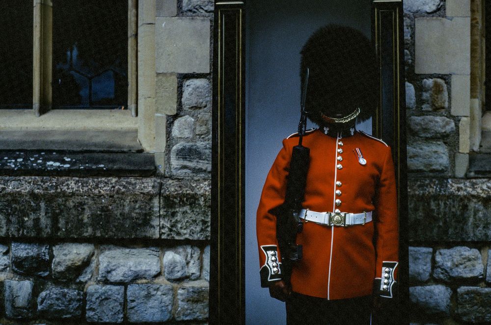 Royal guard in red ceremonial uniform standing at attention in stone doorway.