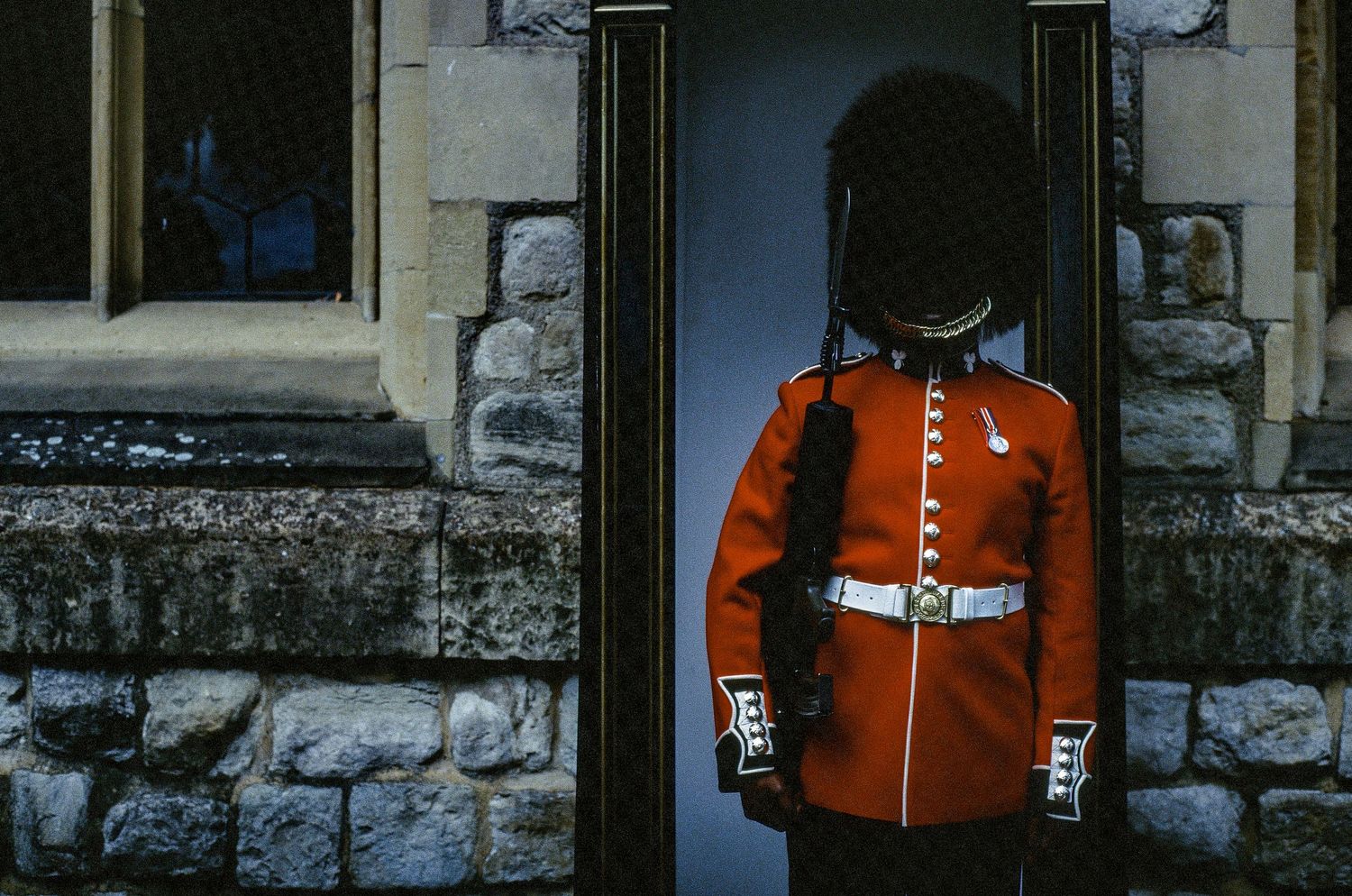 Royal guard in red ceremonial uniform standing at attention in stone doorway.