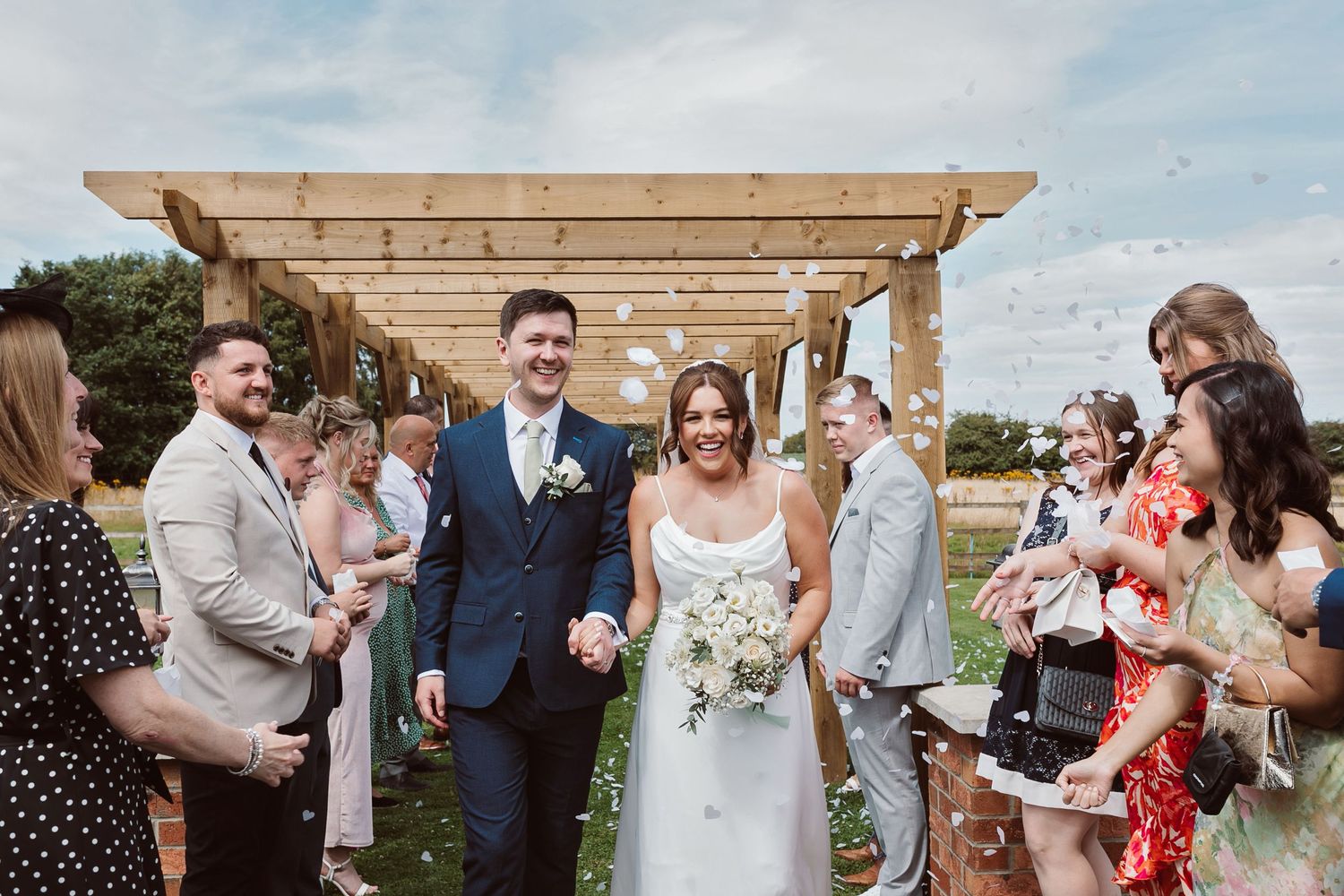 Wedding party celebrates with newlyweds under wooden pergola outdoors. Photographer. Hull. East Yorkshire. Photography