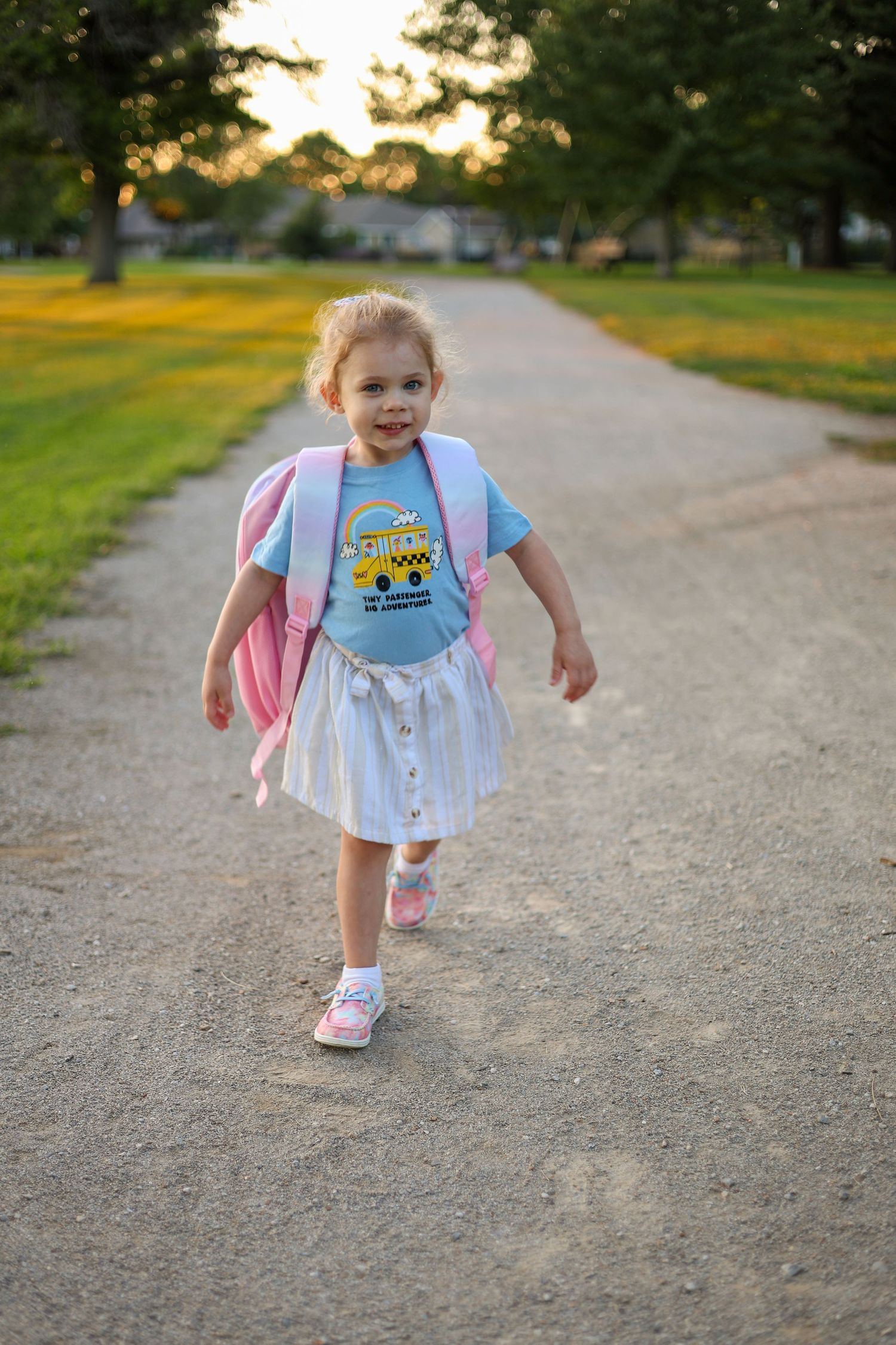 Child walks down path wearing backpack and Minions t-shirt during golden hour.