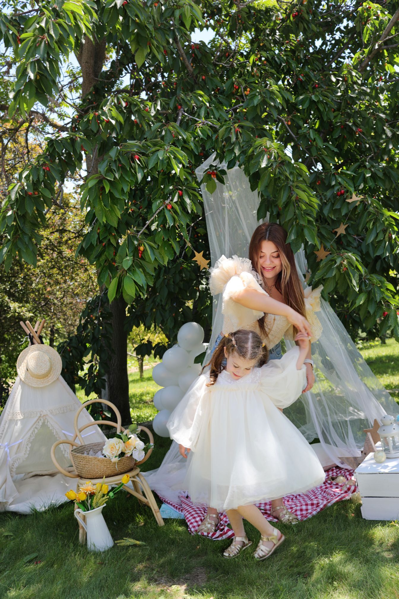 Outdoor tea party scene with white dresses and picnic setup under fruit tree.