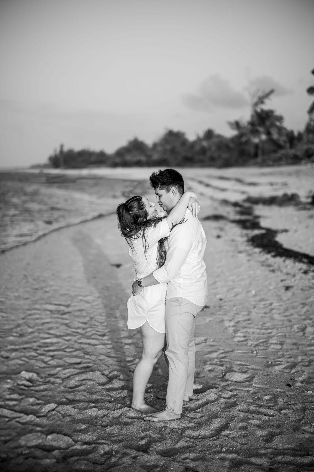 A romantic couple embracing on a sandy beach with palm trees in the background.
