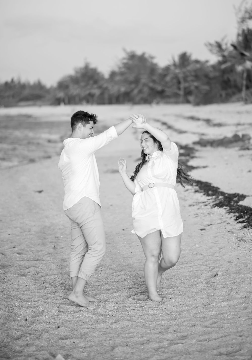 A playful couple dancing together barefoot on a tropical beach.